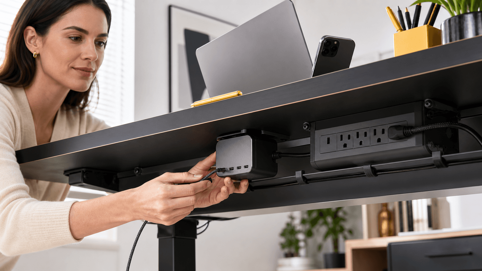 Under-desk view of a black GaN charger and short USB-C cables neatly tied to a light wood desk frame.