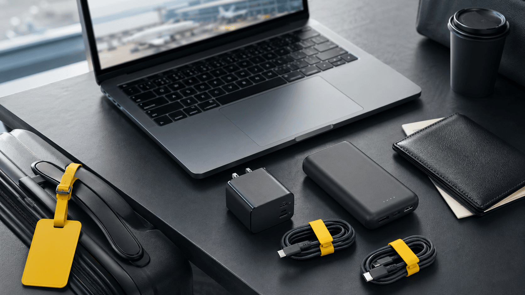 Silver MacBook Pro beside a compact white USB-C charger and cables on a sunlit desk with a world map backdrop