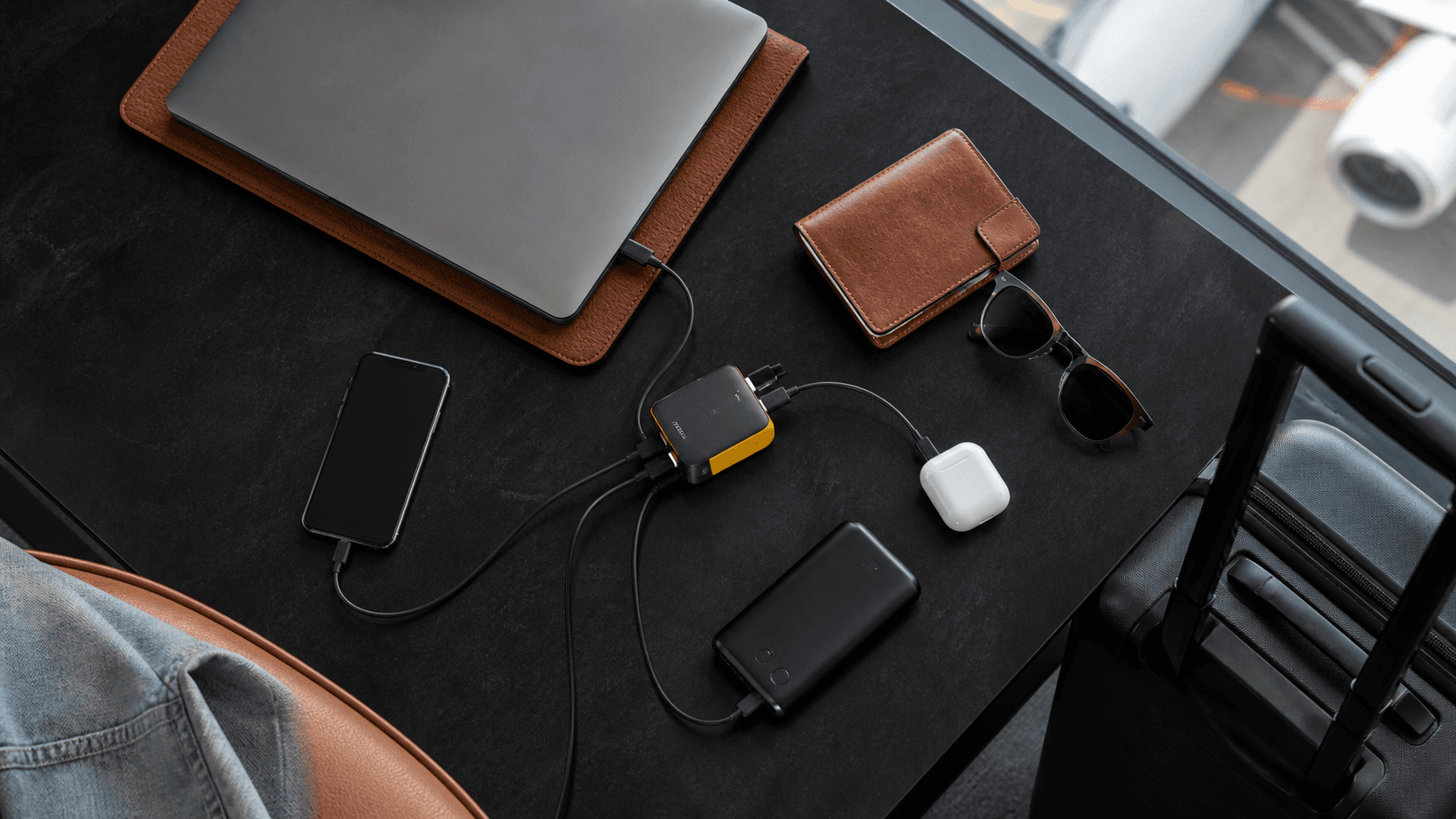 Compact white multiport charger with cables beside a laptop and phone on a sunlit wooden desk.
